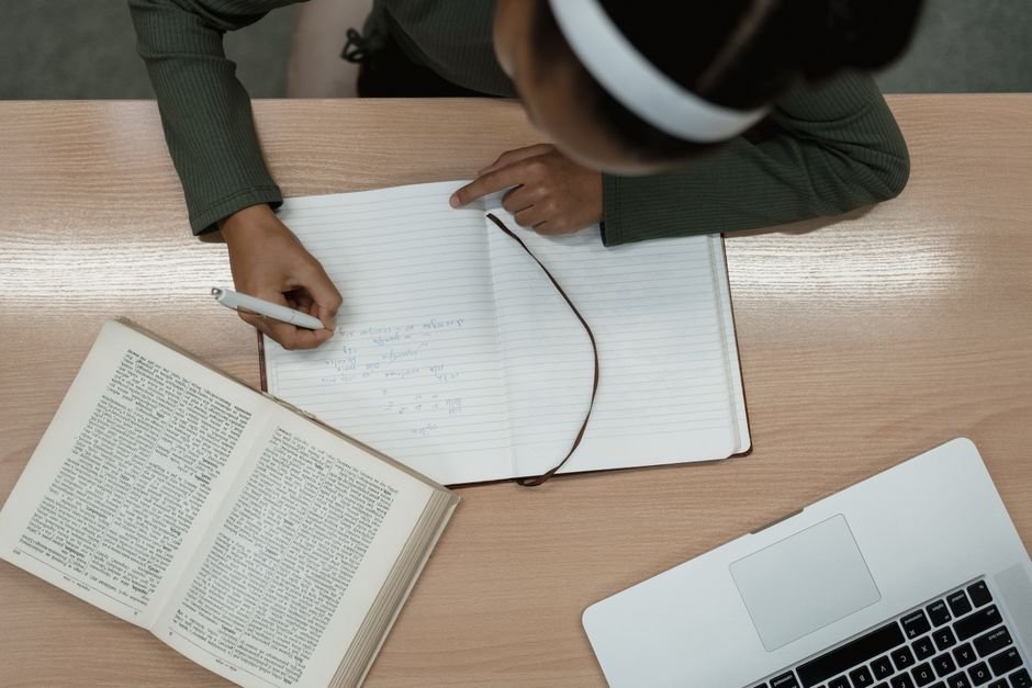 Person studying with a laptop, open book and handwritten notes - hands-on practice of AI skills for DBAs